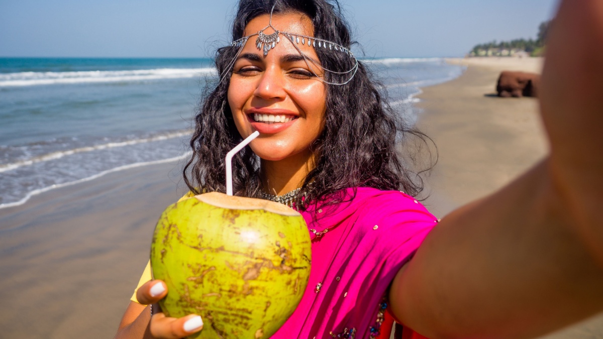 beautiful indian woman taking a portrait selfie photo on the camera phone in pink stylish sari ,toothy white smile sun summer by sea goa. healthy eating concept Indian Ocean bay.