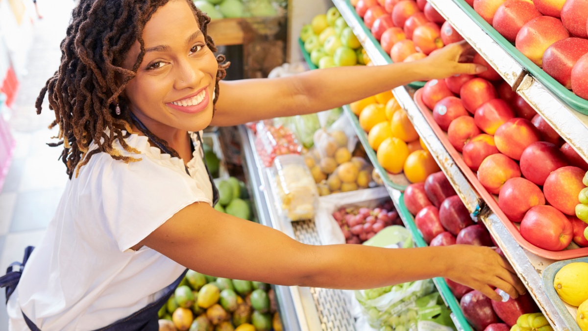 Pretty smiling Black woman working at fruit department at grocery store.