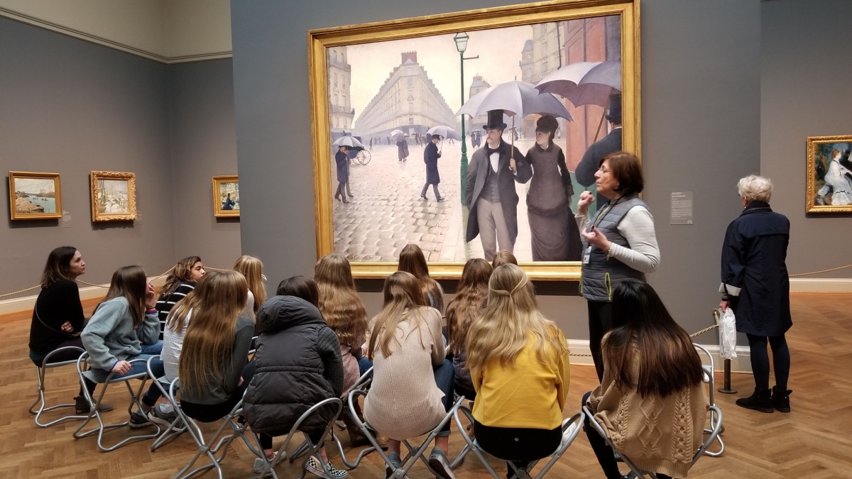 Shown here is a group of students learning about Paris Street; Rainy Day a large 1877 oil painting by the French artist Gustave Caillebotte.