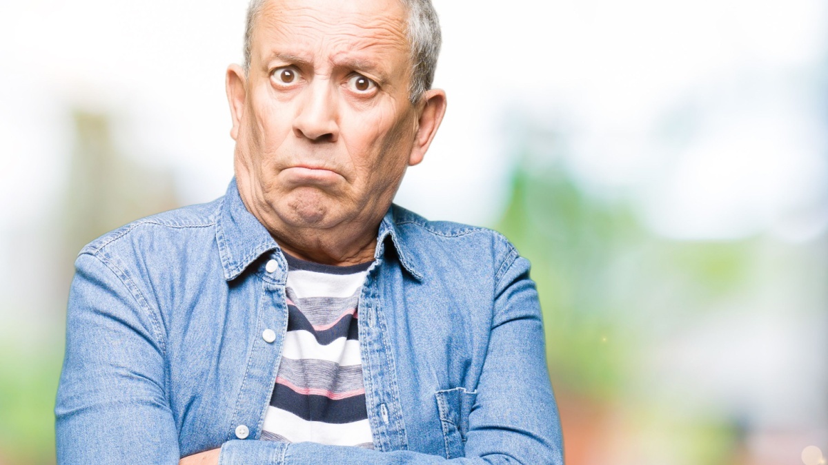 Handsome senior man wearing denim jacket skeptic and nervous, disapproving expression on face with crossed arms.