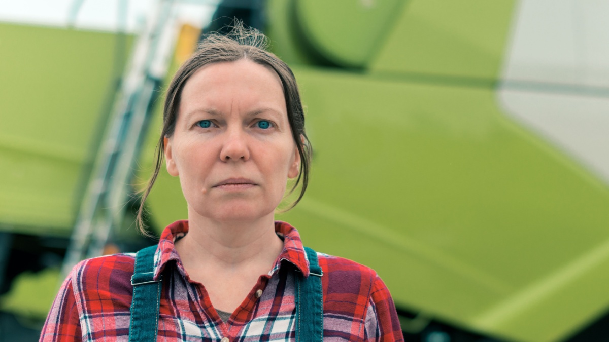 Female farmer posing in front of combine harvester. Serious woman farm worker with agricultural machinery ready harvest crops.