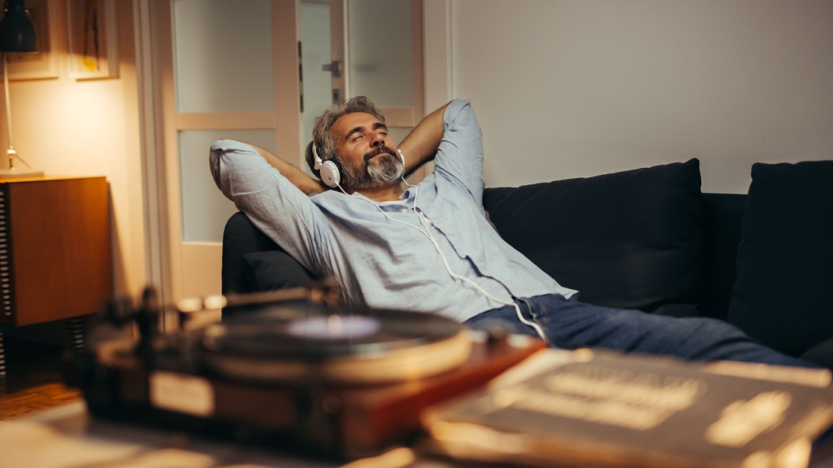 mid aged man listening music with headphones on record player, relaxed in sofa at his home