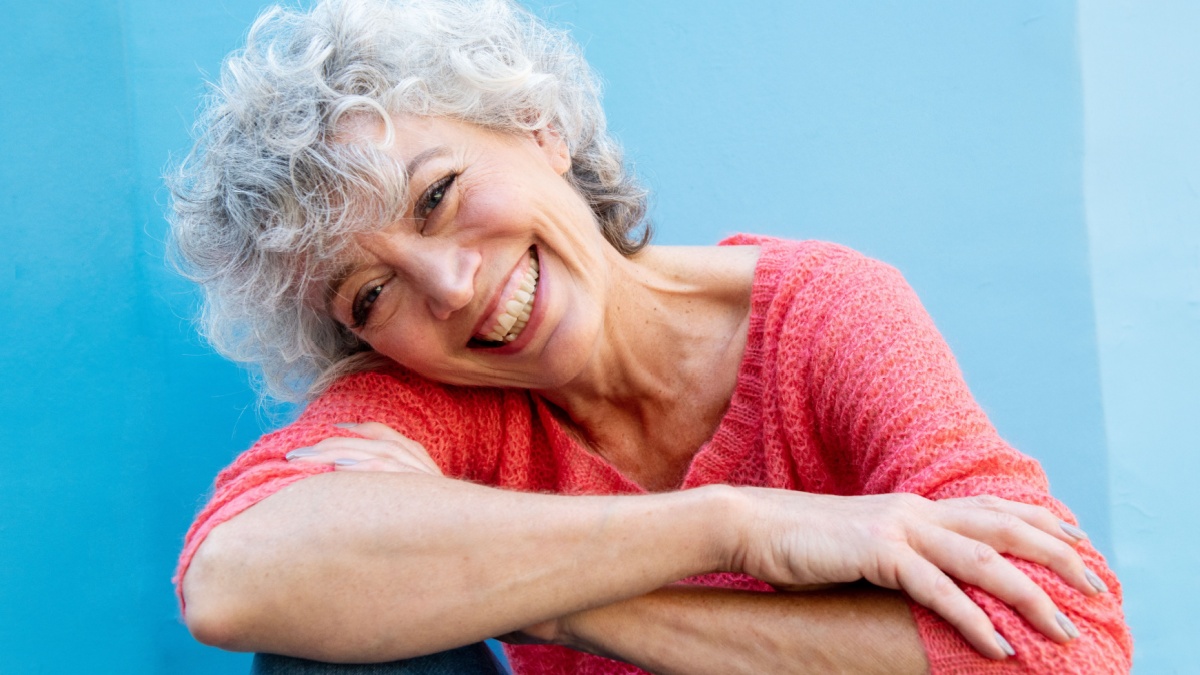 Close up portrait of smiling older woman by blue wall.