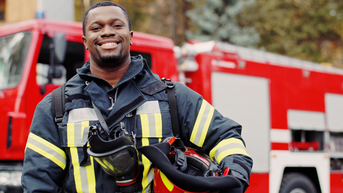 Firefighter portrait on duty. Photo of happy fireman with gas mask and helmet near fire engine