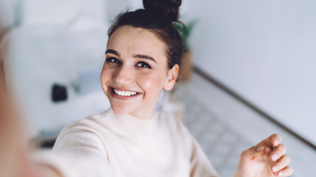 Good mood lady with expansive smile enjoying started weekends and taking selfie on mobile phone on blurred background.