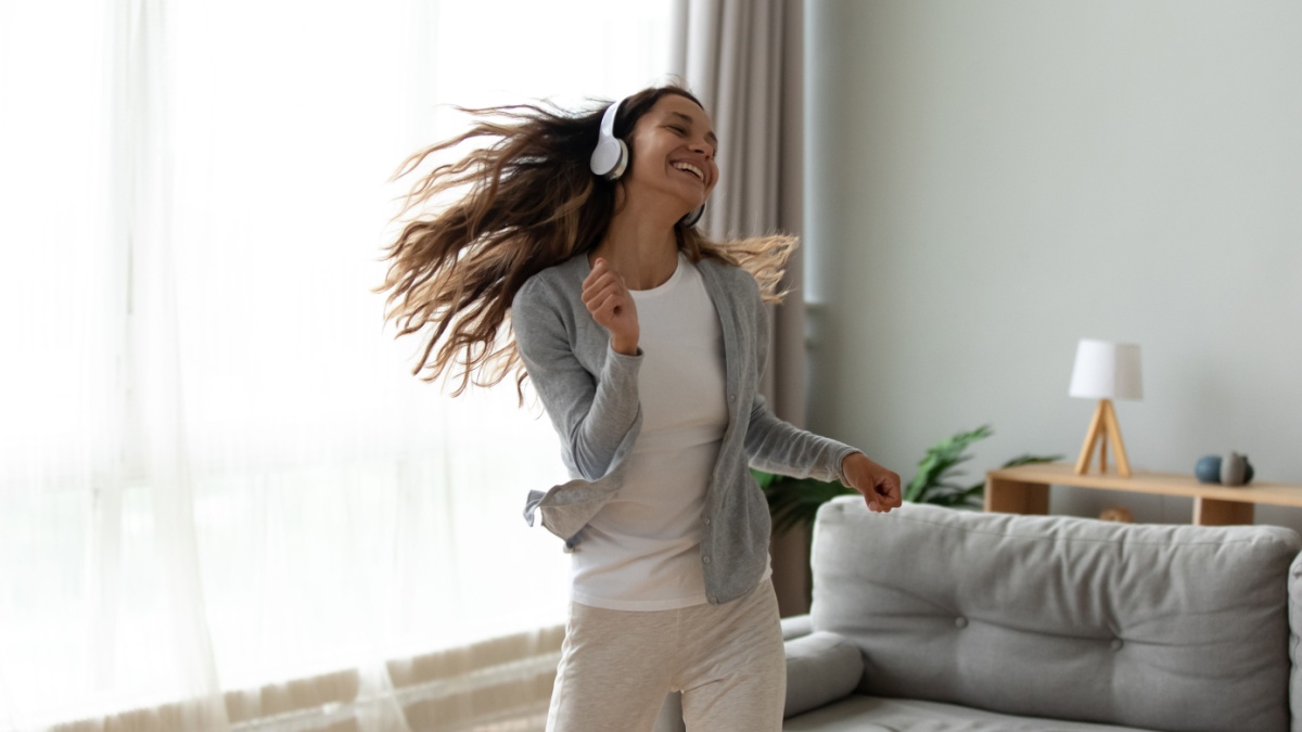Overjoyed millennial girl wearing headphones have fun moving listening to music relax in living room, happy young woman in earphones dance enjoy leisure weekend at home, stress free concept