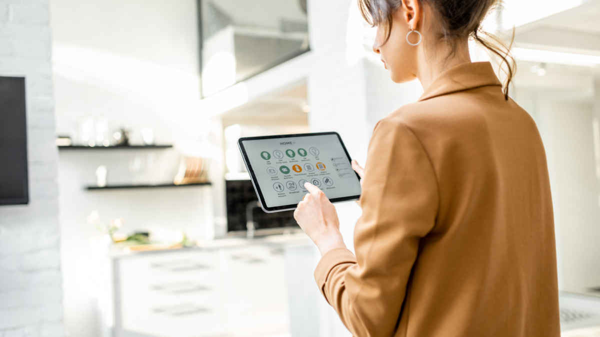 Woman controlling smart home devices using a digital tablet with launched application in the white living room. Smart home concept
