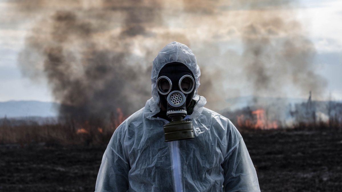 A man in a gas mask in a chemical protective suit shrouded in smoke is walking in a dangerous radioactive zone. A Stalker soldier. Post-Apocalypse. Nuclear war. Environmental disaster.