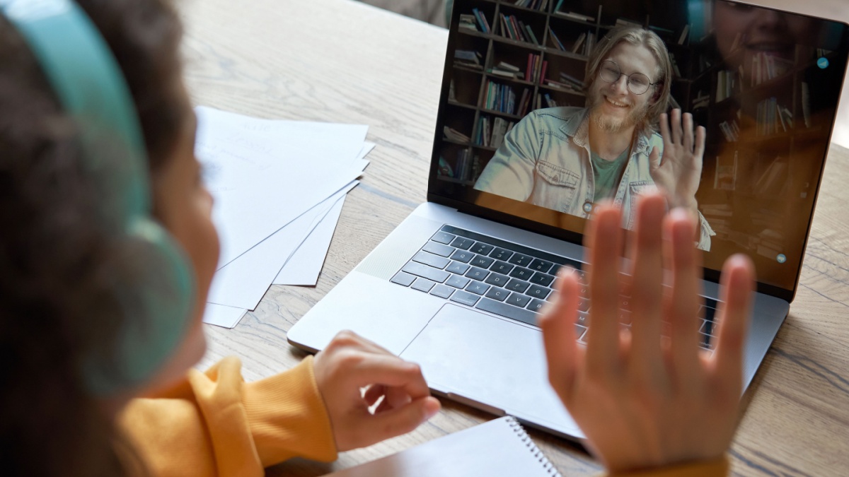 Hispanic teen girl school college student distance learning waving hand studying with online teacher on laptop screen. Elearning zoom video call, videoconference class with tutor. Over shoulder view.