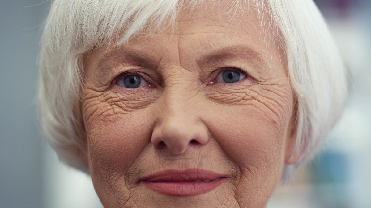 Close up of the Caucasian old happy and cheerful lady with grey short hair looking straight to the camera and smiling. Indoor.