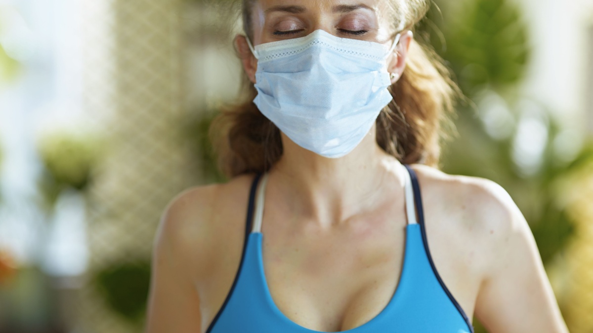Life during coronavirus pandemic. fit middle age woman in sport clothes with medical mask catching breath after exercise.