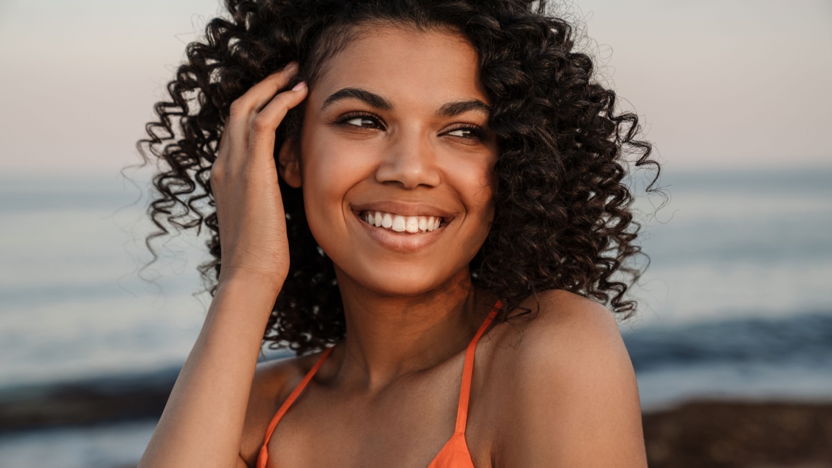 Image of amazing pretty smiling young african woman walking at the beach outside.