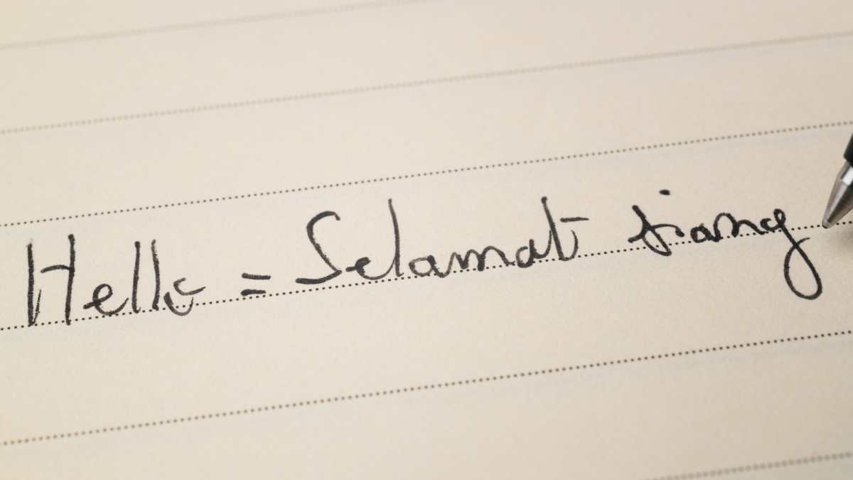 Beginner Indonesian language learner writing Hello formal word Selamat siang for homework on a notebook