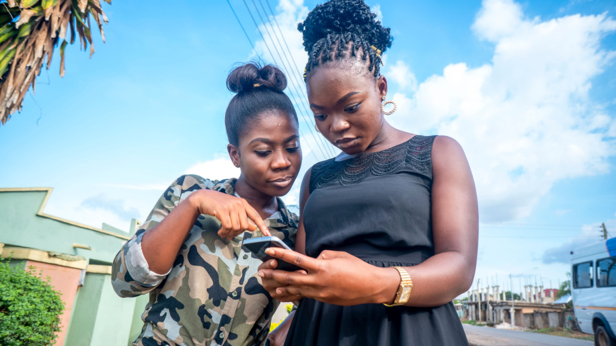 Two beautiful African women looking curiously on smartphone in hand.