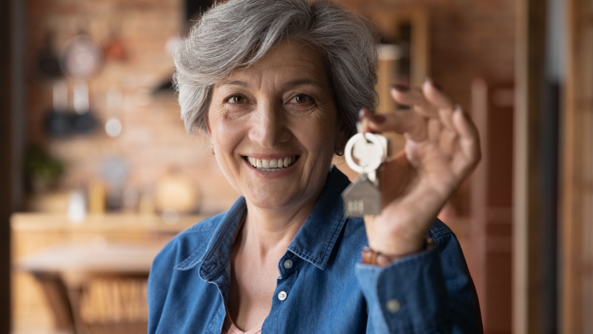 Head shot portrait smiling mature woman holding key from new home, own apartment, looking at camera, excited mature female owner moving into new house, satisfied client customer purchase real estate.