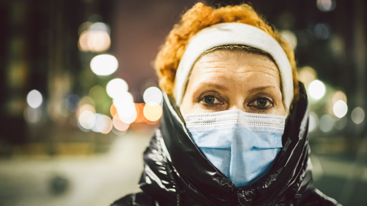 Mature woman with face mask protection, elderly woman in face mask due to air pollution in the evening city as background, sick old people.