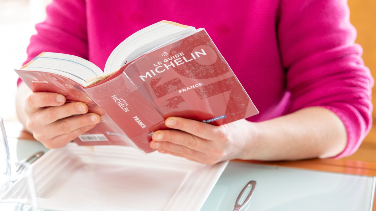 Woman reading Red Michelin guide book which reviews restaurants.