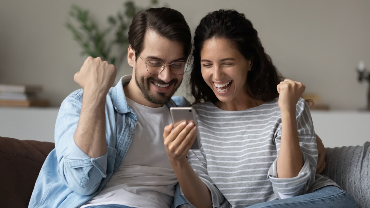 Excited joyful family couple using smartphone, looking at screen, making winner yes gesture together.