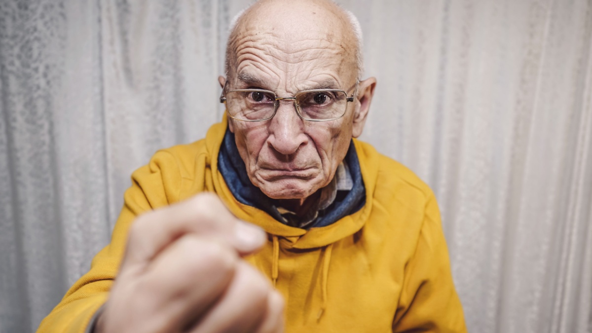 Portrait of angry caucasian man wearing eyeglasses and showing big fist standing at home indoor.
