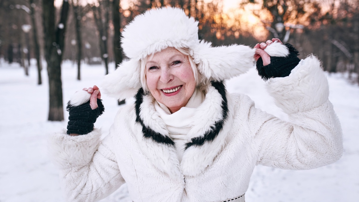 senior woman in white hat and fur coat enjoying winter in snow forest.