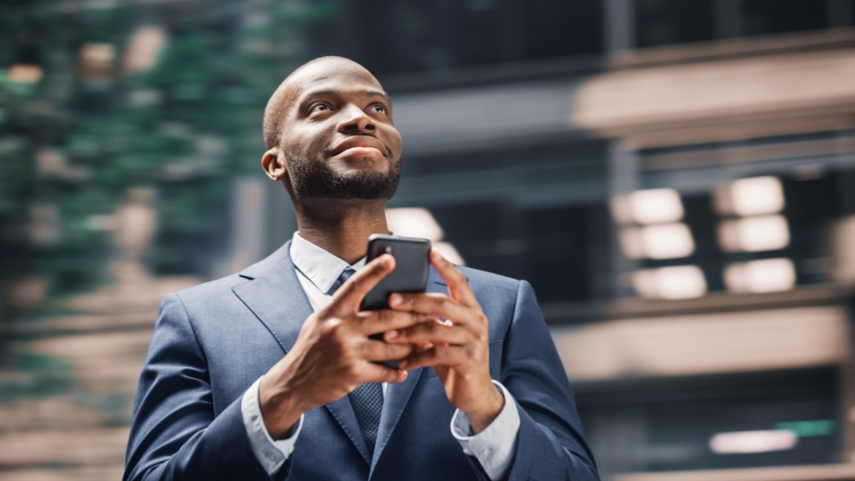 Street Shot: Portrait of Happy Black Businessman Using Smartphone in City.