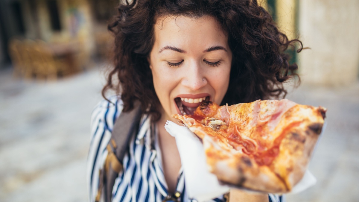 Beautiful young tourist woman eating a slice of pizza outdoor.