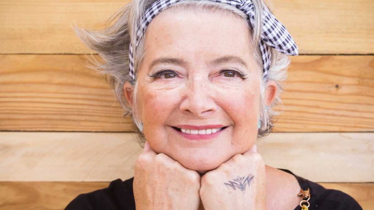 Porttait of young old senior woman smiling and posing for a picture with tattoo on hand. Trendy mature woman with make up.