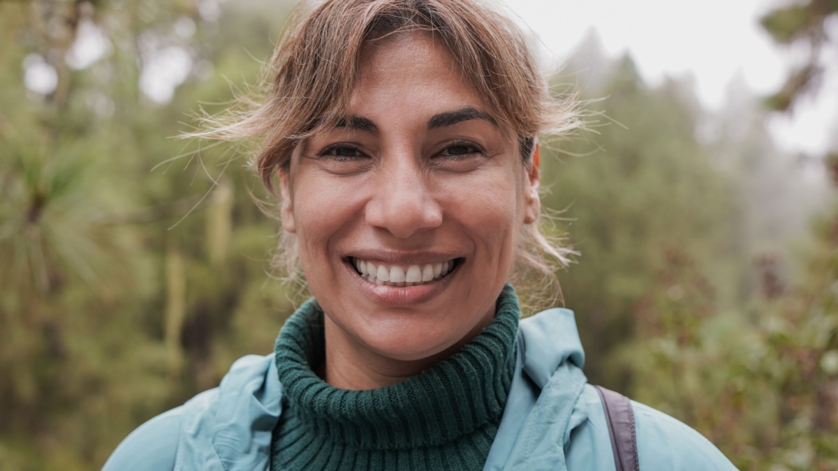 Mature latin woman smiling on camera during trekking day in nature forest.