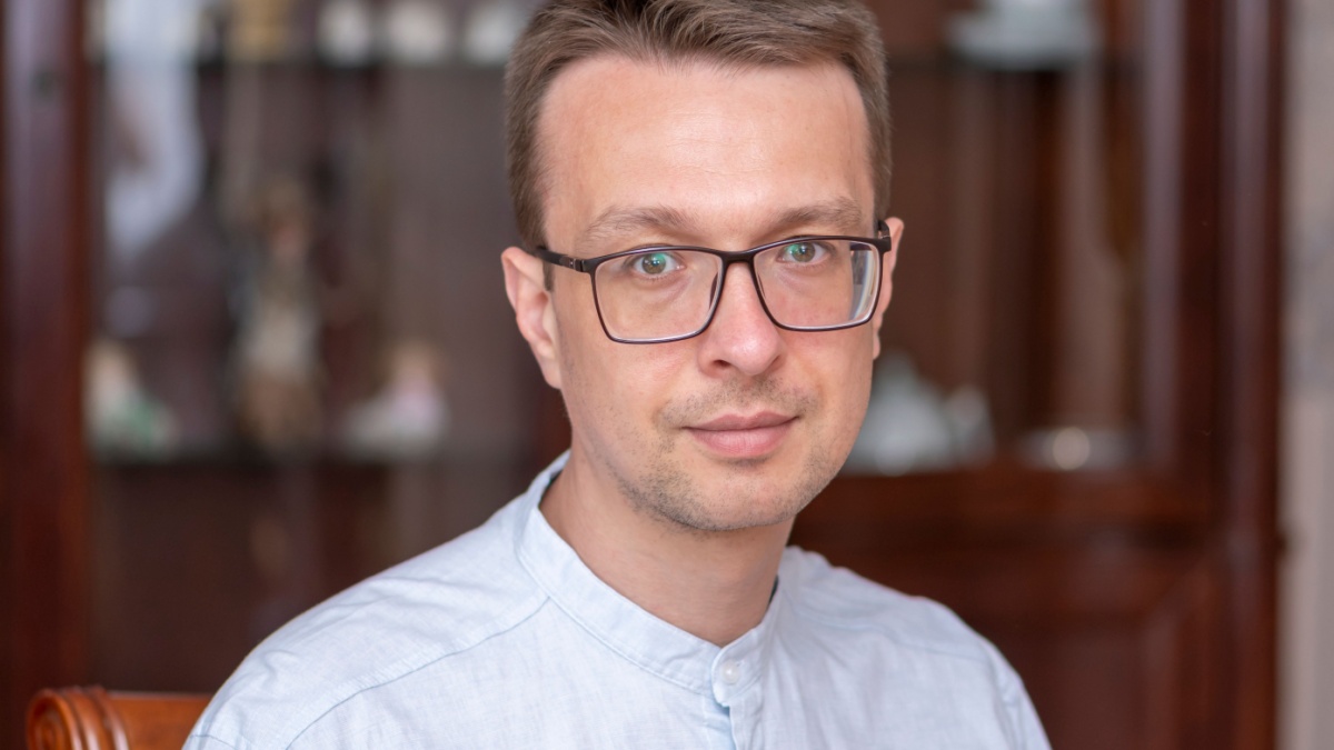 Portrait of a middle-aged man in glasses and a light shirt on a blurred background in the apartment.