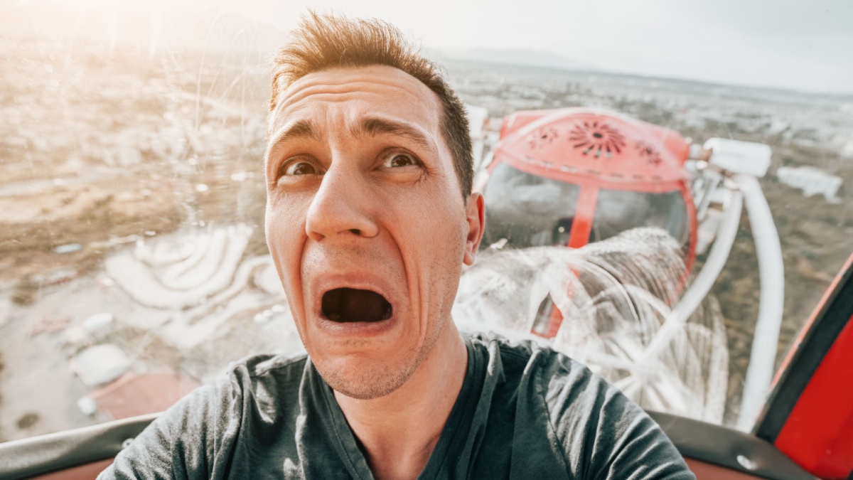 A guy with acrophobia or fear of heights screams with funny emotions on his face from the view from a high Ferris wheel in an amusement park.