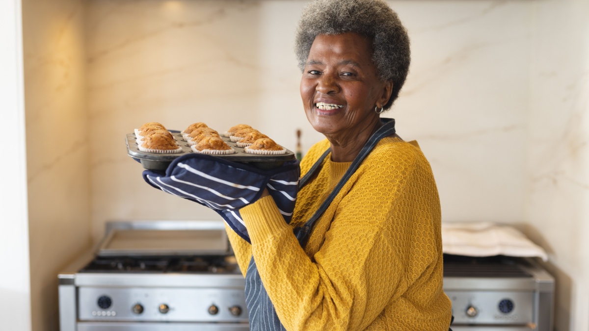 Image of happy african american senior woman with tray full of freshly baked cupcakes.