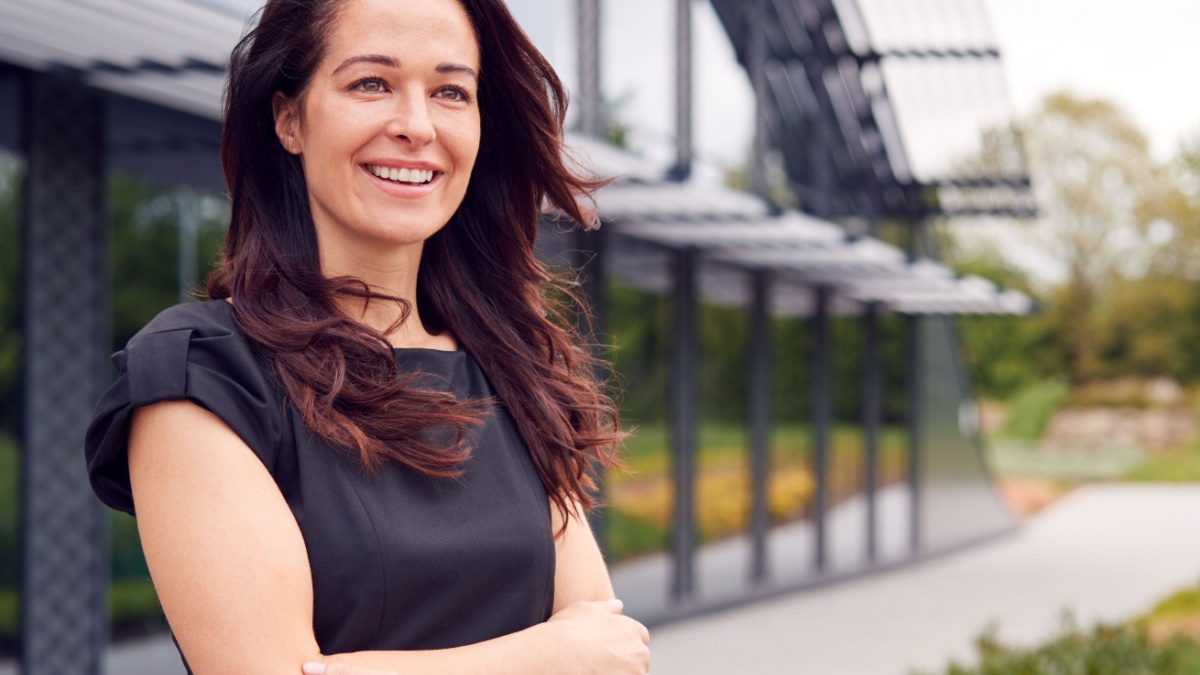 Portrait Of Smiling Mature Businesswoman CEO Chairperson Standing Outside Modern Office Building.