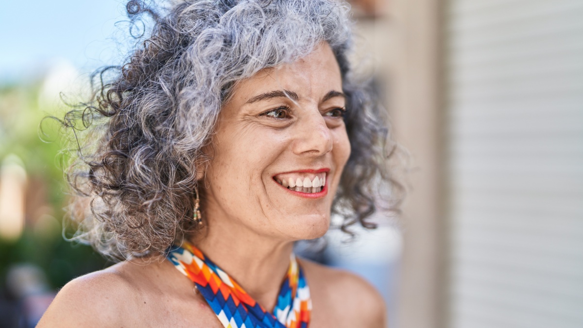 Middle age grey-haired woman smiling confident looking to the side at street.