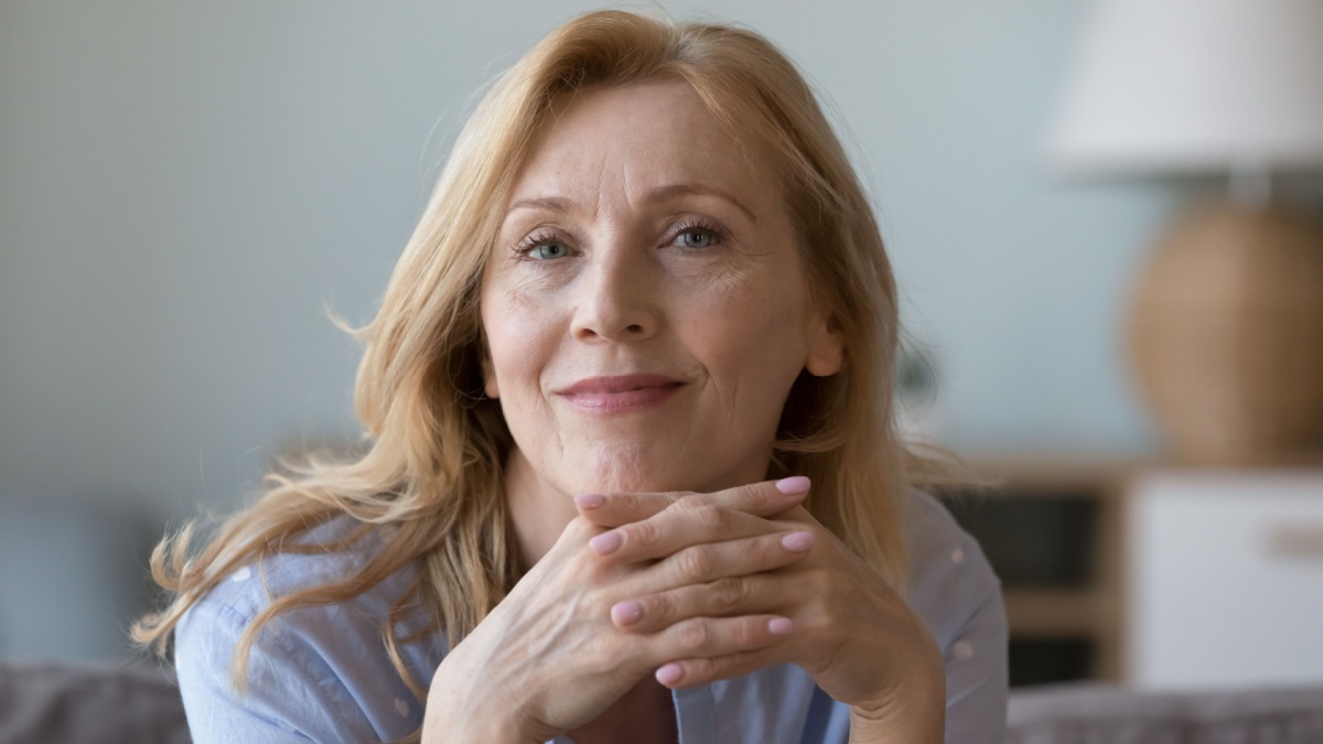Head shot close up portrait attractive middle-aged woman resting on cozy sofa alone at home staring at camera.