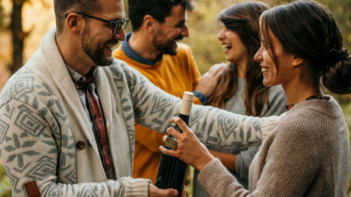 Group of friends welcoming each other. The host welcomed and hugged their friends who came to dinner with a wine bottle smiles and hugs.