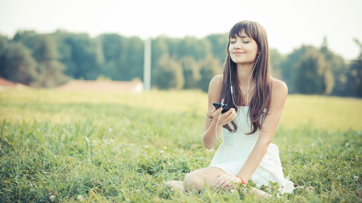 beautiful young woman with white dress listening music in the park