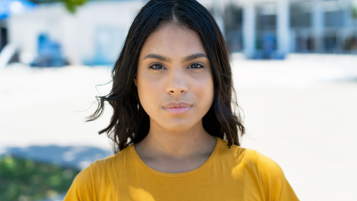Portrait of serious mexican young adult woman with long black hair outdoor in summer in city.