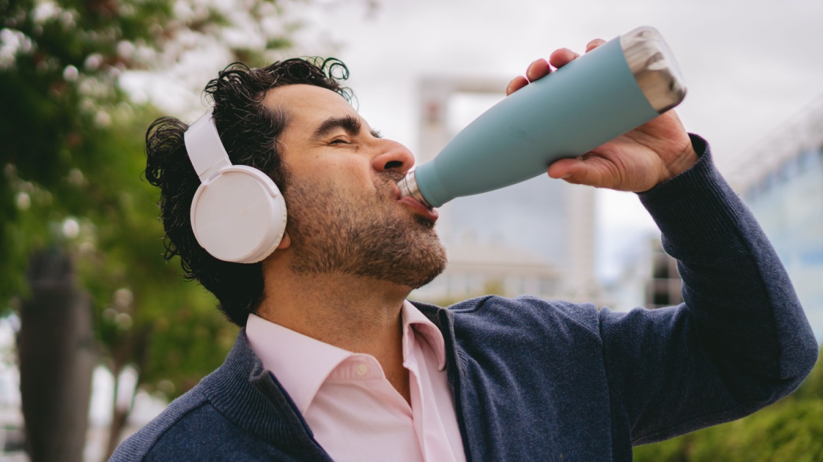 Middle-aged Latin man with headphones drinking water from a reusable water bottle.