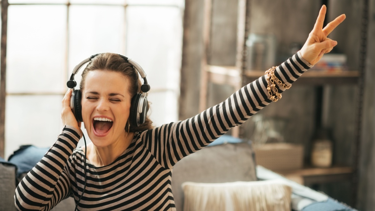 Cheerful young woman listening music in headphones in loft apartment