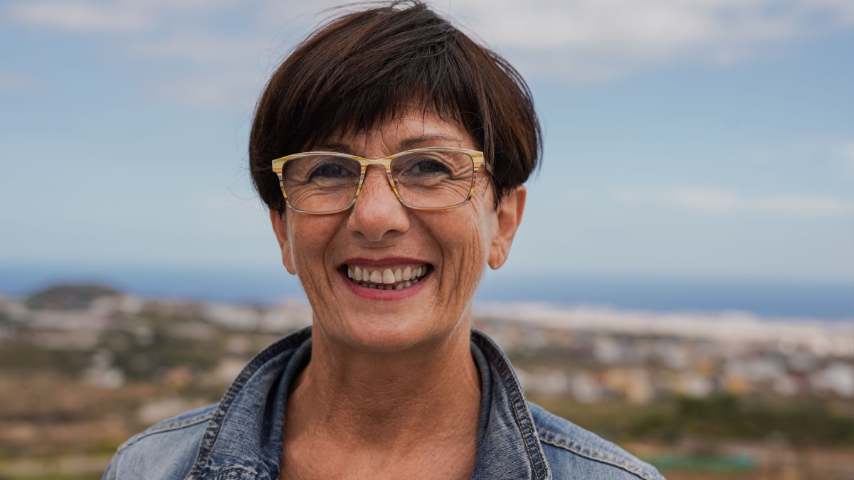Happy senior woman smiling on camera at house rooftop with ocean view in the background - Joyful elderly concept.
