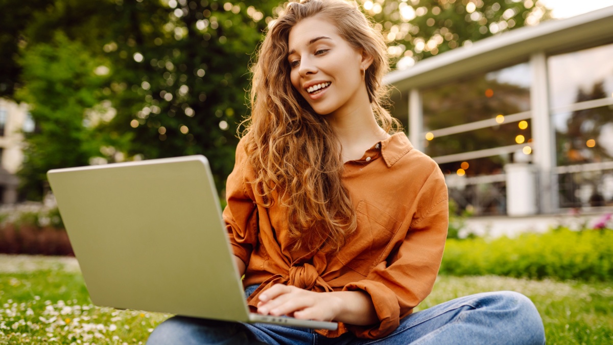 Smiling young woman with a laptop working or studying online outdoor.