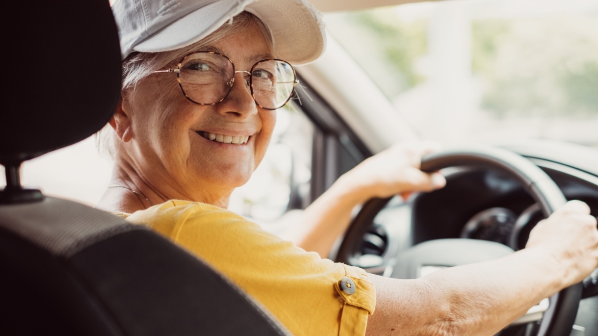 Close up portrait of senior looking female with glad positive expression, being satisfied with unforgettable journey by car, sits on driver`s seat, enjoys music.