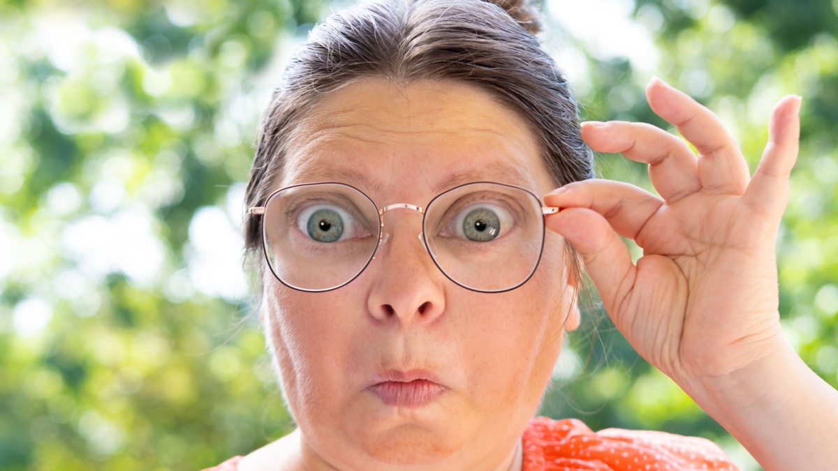 close up female face, funny woman in glasses looks through lenses in surprise, concept unexpected object observation, mental human health, regular eye.