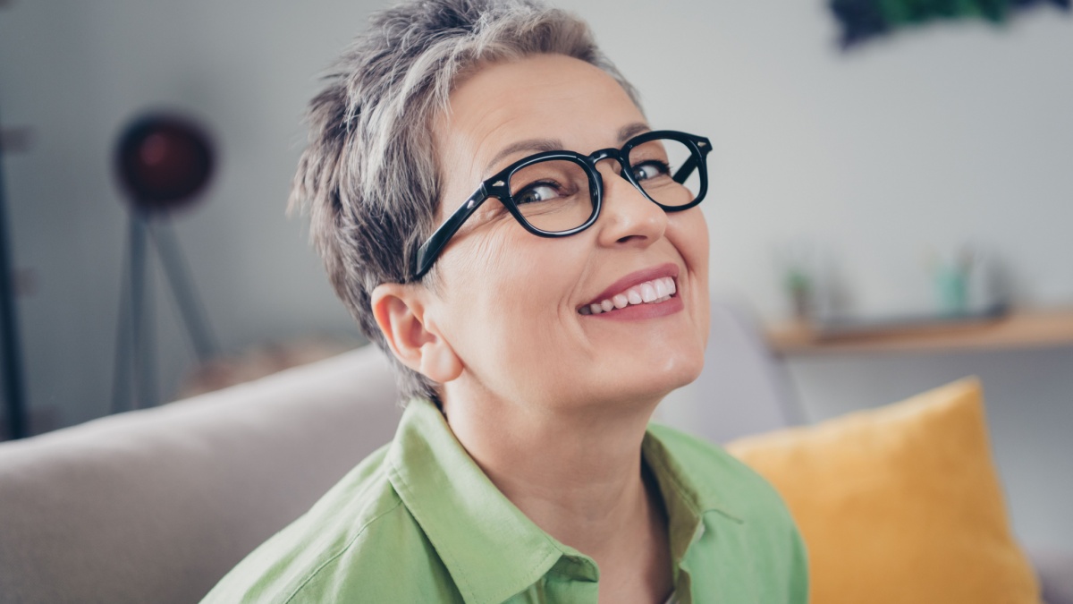 Portrait of attractive toothy smiling businesswoman wearing eyeglasses khaki shirt spending free time after working hours indoors.
