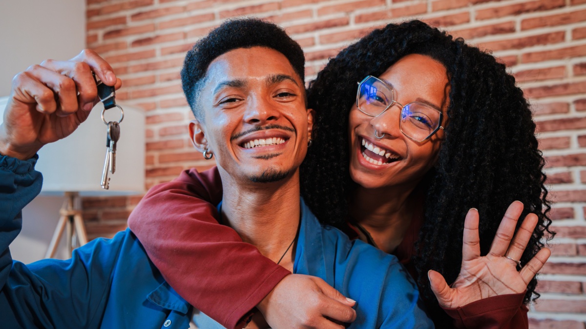 Young african american couple showing keys of their first house after purchase and moving to new home together.