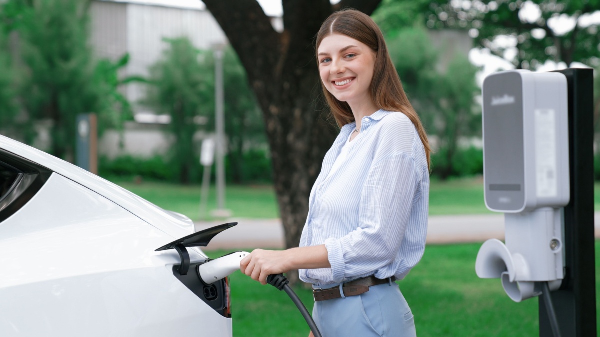 Young woman recharging battery for electric car during road trip travel EV car in natural forest or national park.