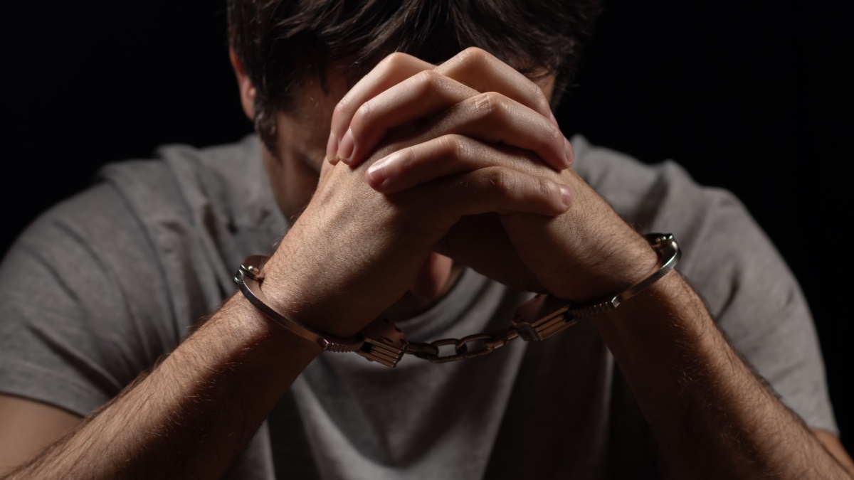 Handcuffed man covering his face with his hands.