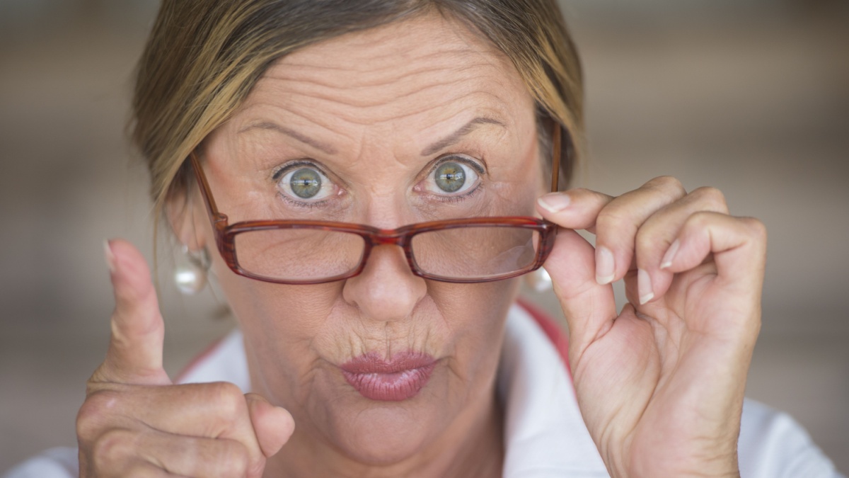Portrait smart attractive mature business woman or dominant teacher with glasses and angry upset expression, blurred background.