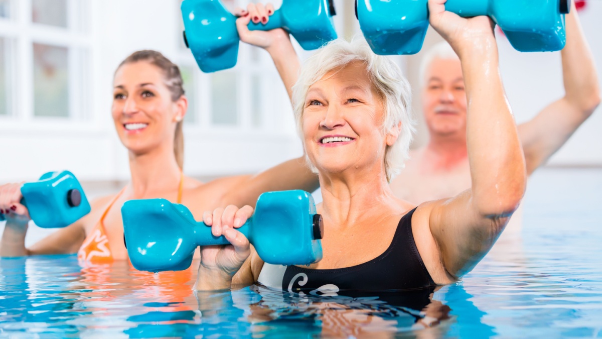 People young and senior in water gymnastics physiotherapy with dumbbells.