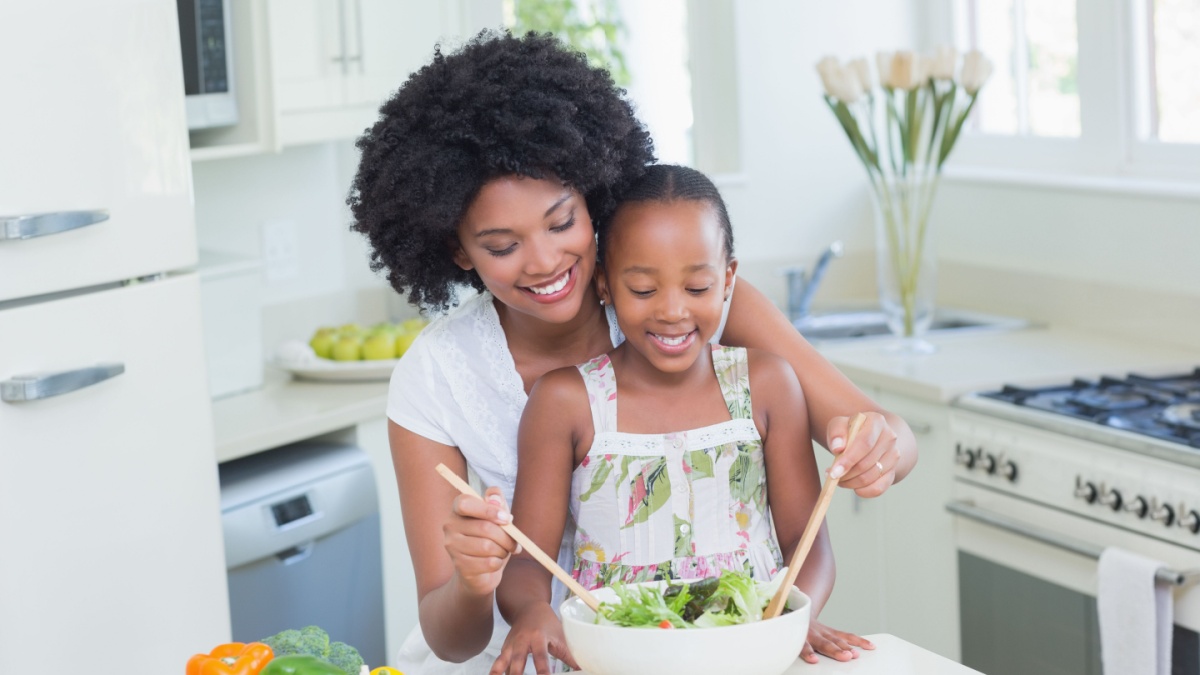 Mother and daughter making a salad together at home in the kitchen.